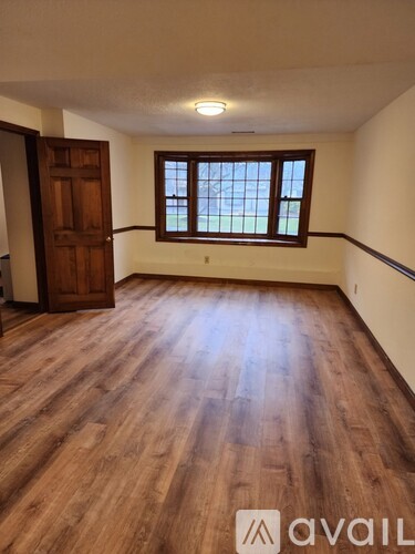 A room with wooden flooring and a window with a view of trees.