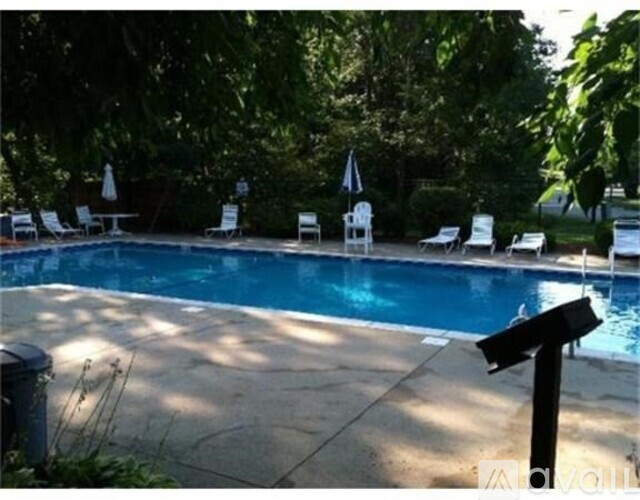 A pool surrounded by trees and chairs.