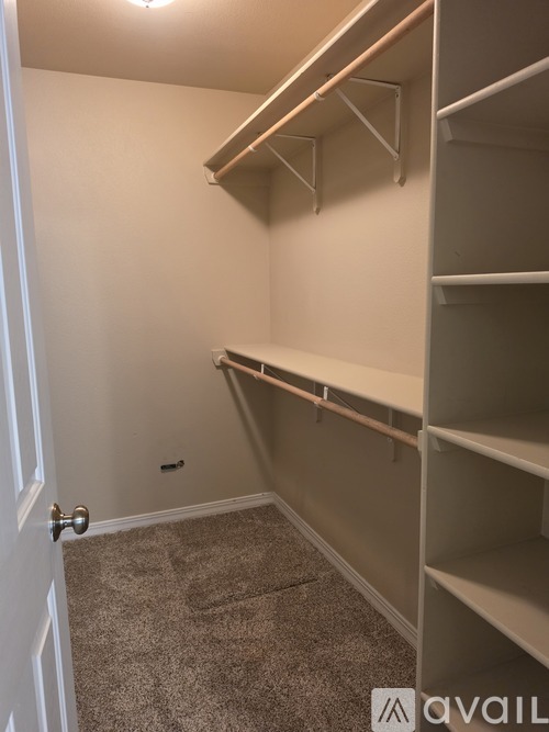 A white door is on the left of a room with a carpeted floor and a wall with a shelf.