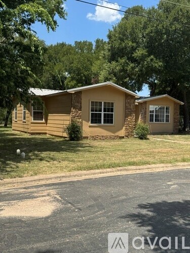 A house with a brown siding and a tan roof is surrounded by green trees.