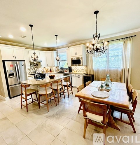 A kitchen with a table and chairs in the foreground and a fridge, microwave, and dishwasher in the background.