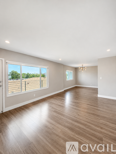 A spacious room with wooden flooring and a large window overlooking a wooden fence.