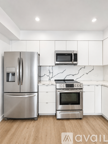 A kitchen with a stainless steel refrigerator and oven, white cabinets, and a wooden floor.