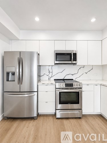 A kitchen with a stainless steel refrigerator and oven, white cabinets, and a wooden floor.