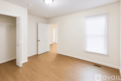 A room with wooden floors and white walls, with a window covered by white blinds.