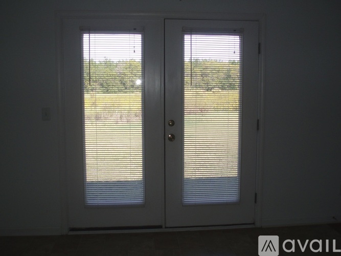 A white double door with blinds is open to a view of a grassy field.