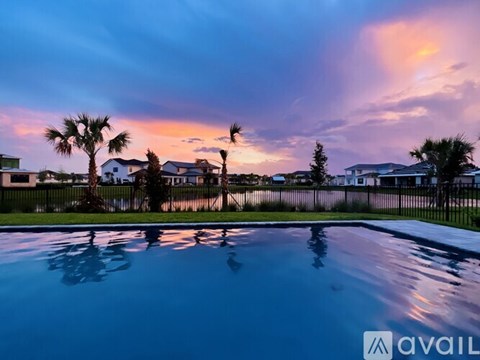 A pool with palm trees and houses in the background at sunset.