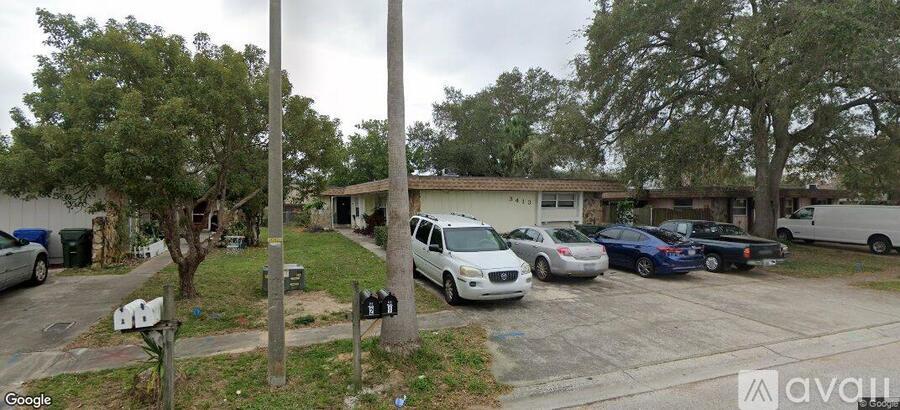 A street view of a residential area with cars parked and a house in the background.