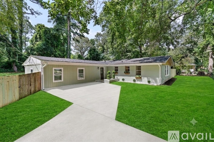 A house with a grey roof and a white fence is surrounded by greenery.