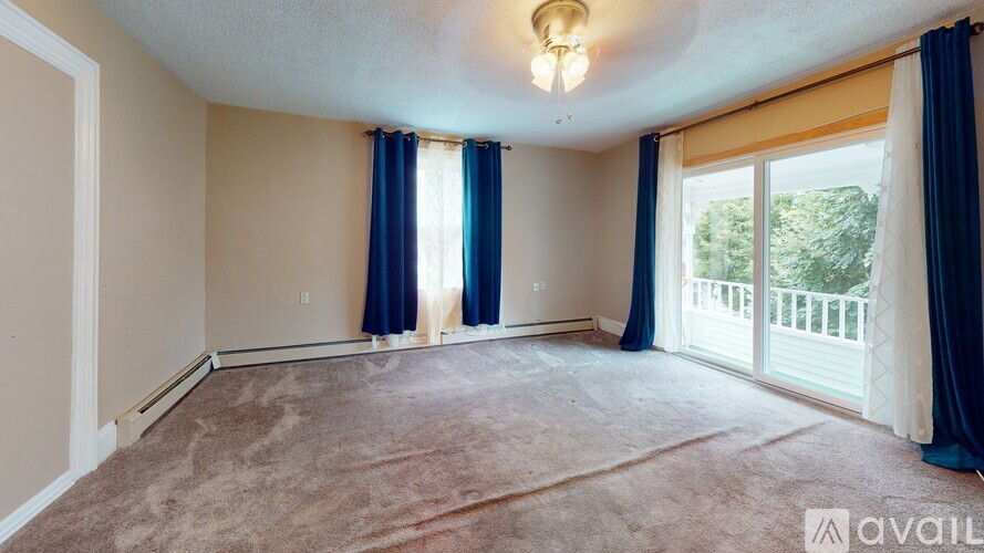 A room with a carpeted floor, a ceiling light, and a sliding glass door leading to a balcony.