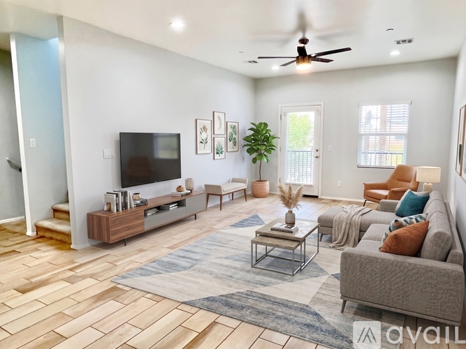 A living room with a grey couch, a wooden floor, and a television on the wall.