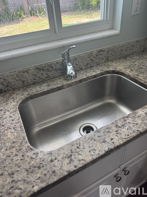 A kitchen sink with granite countertop and a window above it.