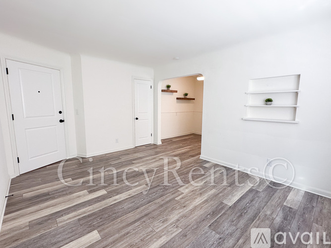 A room with white walls and wooden flooring with a shelf on the wall.