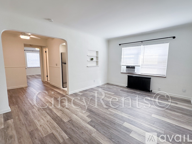 A spacious room with wooden flooring and a large window with blinds.