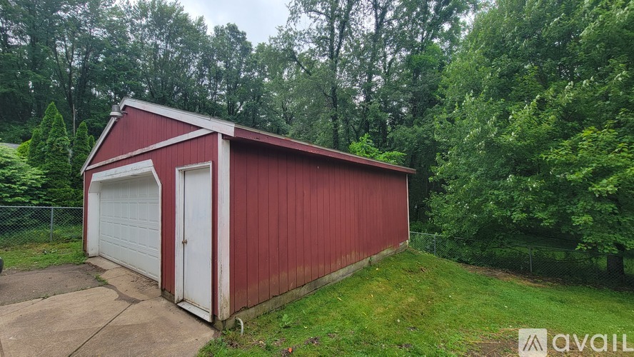 A red garage with a white door is situated in a grassy area with trees in the background.