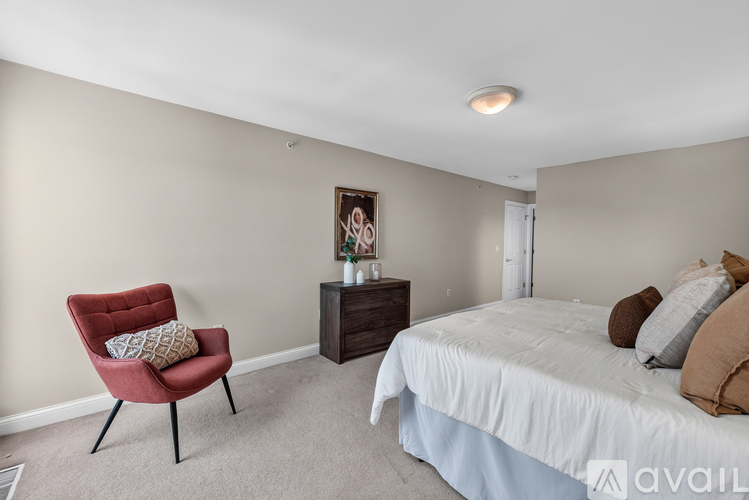 A bedroom with a red chair and a bed with a white sheet.