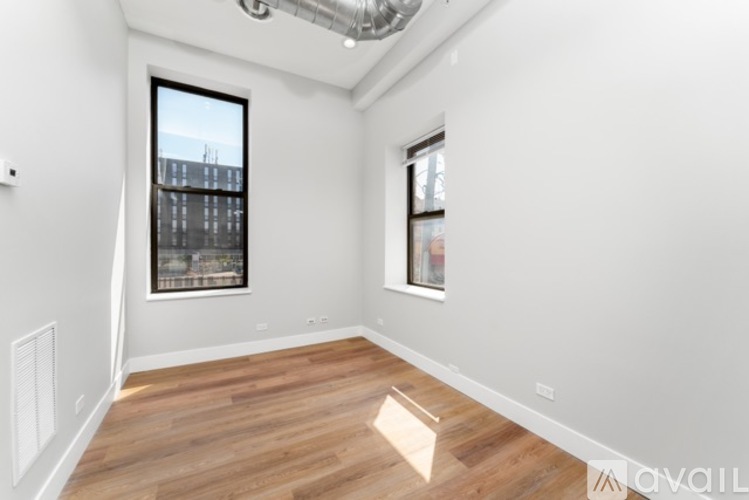 A spacious room with wooden flooring and two windows.
