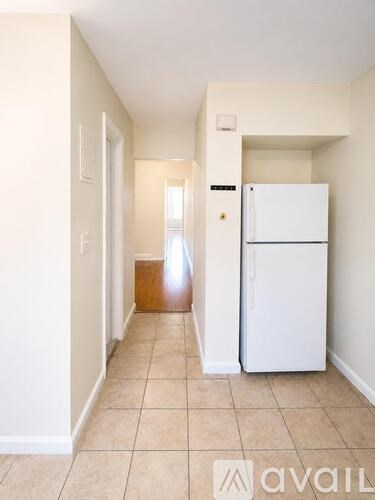 A white refrigerator is in a kitchen with beige tile floors and white walls.