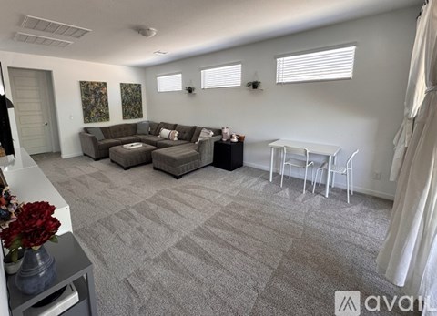 A living room with a grey carpet and a grey couch.