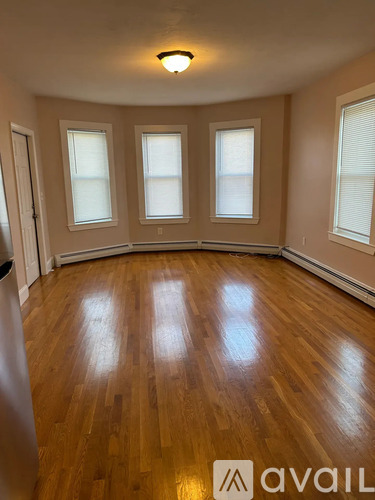 A room with wooden flooring and three windows.