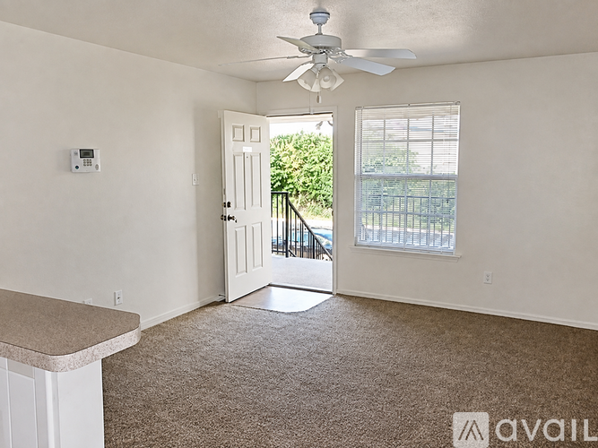 A room with a carpeted floor, a ceiling fan, and a door leading to a balcony.