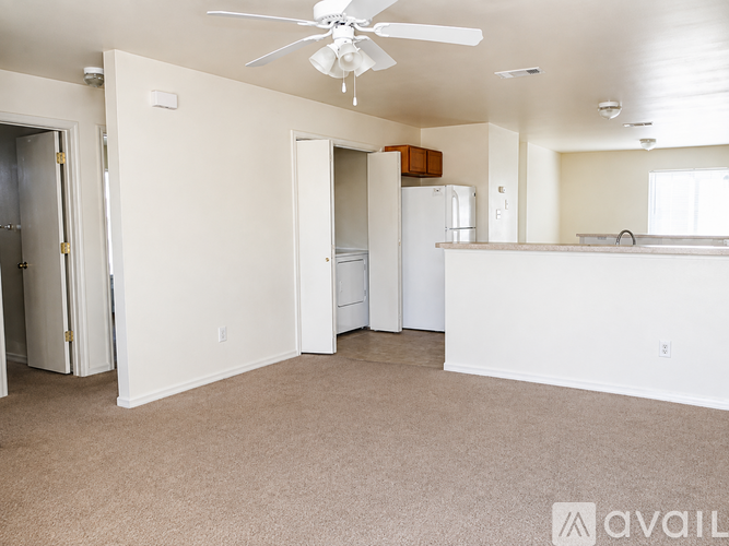 A spacious living room with a fan and a kitchen area in the background.