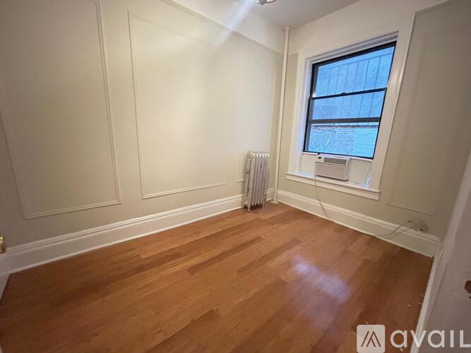 A room with wooden flooring and a window with a view of a building.
