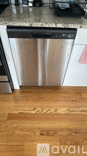 A kitchen with a stainless steel dishwasher and wooden flooring.