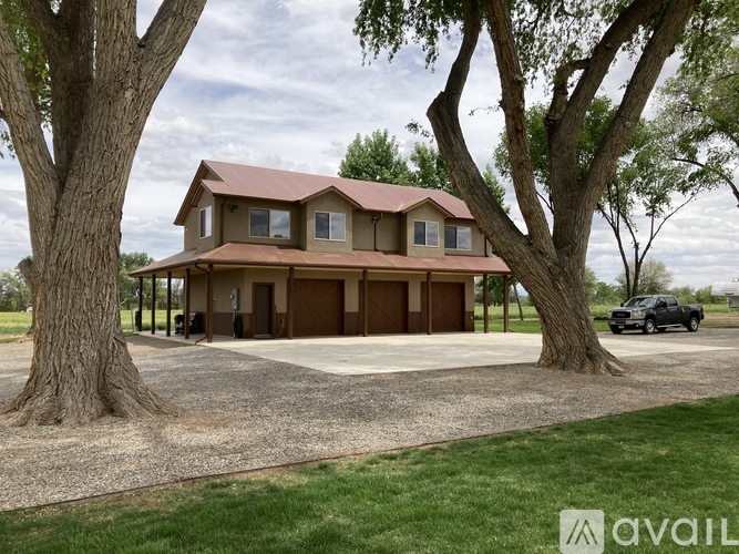 A house with a brown roof is surrounded by trees and has a gravel driveway.