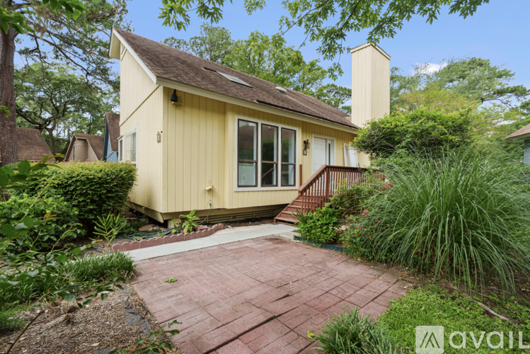 A yellow house with a brown roof and a brick walkway in front.