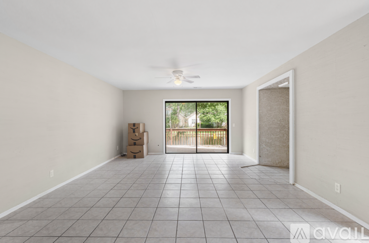A spacious room with tiled flooring and a ceiling fan, leading to a balcony with a view of greenery.