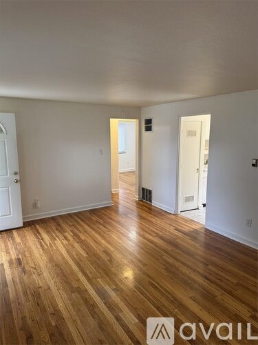 A room with wooden floors and white walls, with a door on the left and another door on the right.