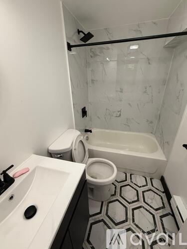 A white sink with a black soap dish and a black faucet is in a bathroom with a toilet and a bathtub.