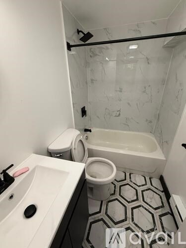 A white sink with a black soap dish and a black faucet is in a bathroom with a toilet and a bathtub.