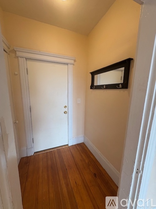 A white door is in a hallway with wood floors and a mirror above it.