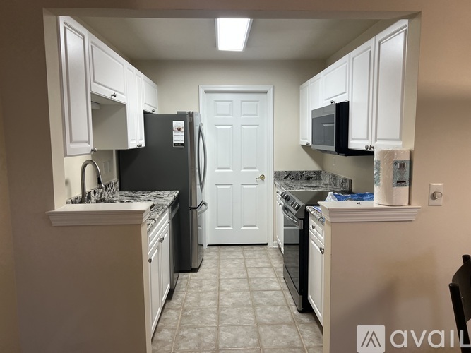 A kitchen with white cabinets and appliances, a black refrigerator, and a white door.