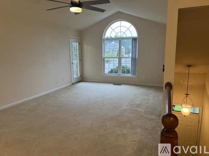A room with a carpeted floor, a ceiling fan, and a large arched window.