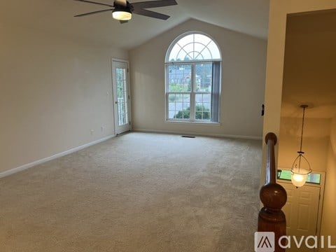 A room with a carpeted floor, a ceiling fan, and a large arched window.