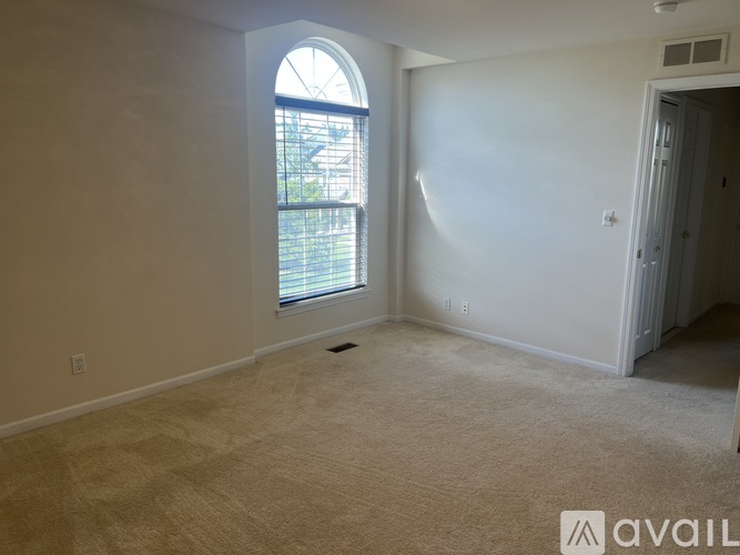 A room with a carpeted floor, a window with a view of trees, and a door leading to another room.