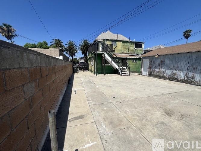A backyard with a concrete patio and a green house in the background.