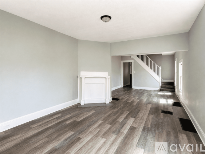 A spacious room with wooden flooring and a staircase in the background.