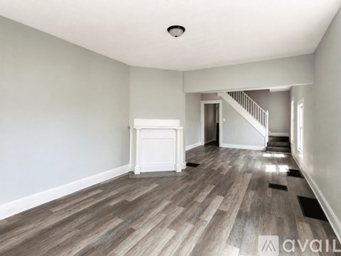 A spacious room with wooden flooring and a staircase in the background.