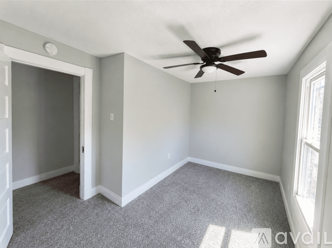 A room with a ceiling fan and a window letting in sunlight.