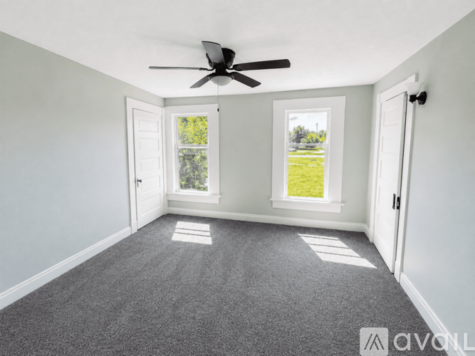A room with a ceiling fan and two windows.