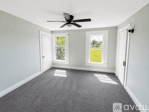 A room with a ceiling fan and two windows.