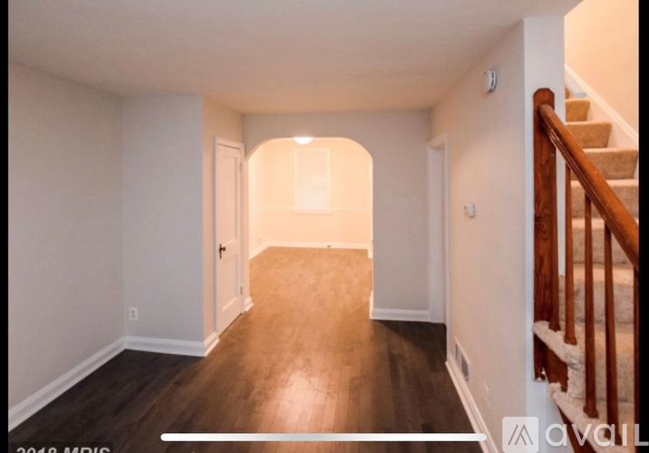 A hallway with wooden floors and a staircase on the right.