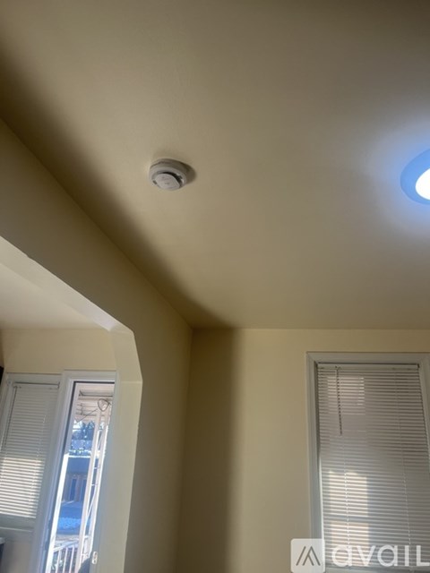 A ceiling with a smoke detector and a window with blinds.