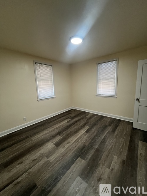 A room with wooden flooring and two windows.
