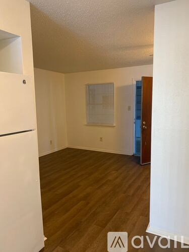 A white refrigerator is in the corner of a room with wood floors and white walls.