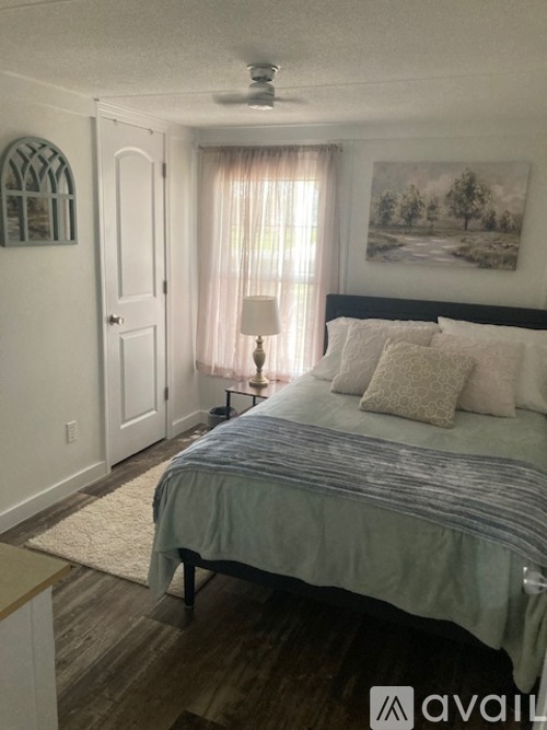 A bedroom with a bed, a window with curtains, a ceiling fan, and a painting on the wall.